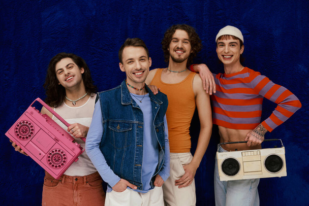 four joyous handsome stylish gay men in casual outfits posing with tape recorders, pride month - Photo, Image