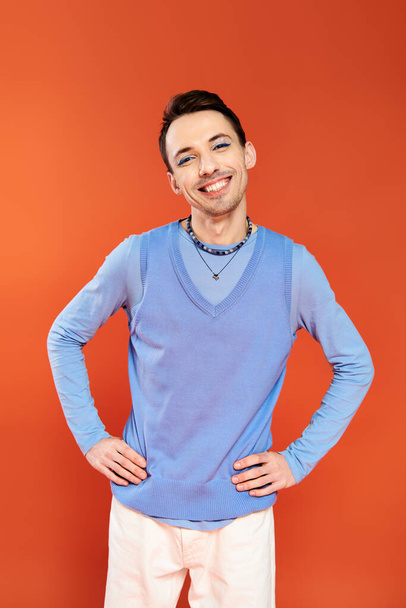 mery attractive stylish gay man with vibrant makeup posing on orange backdrop, pride month - Foto, imagen