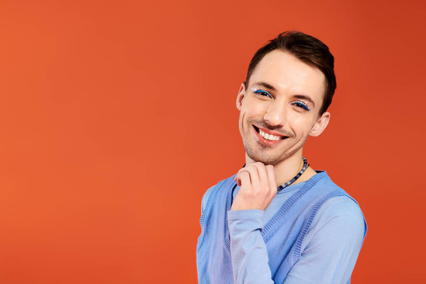 весёлый привлекательный стильный гей с ярким макияжем, позирующий на оранжевом фоне, месяц гордости - Фото, изображение
