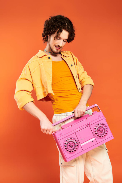 bien parecido alegre gay hombre posando alegremente con cinta grabadora en naranja telón de fondo, orgullo mes - Foto, imagen
