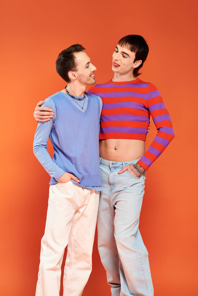 χαρούμενους γκέι φίλους με ζωηρό μακιγιάζ ποζάρουν μαζί σε πορτοκαλί φόντο, μήνα υπερηφάνειας - Φωτογραφία, εικόνα