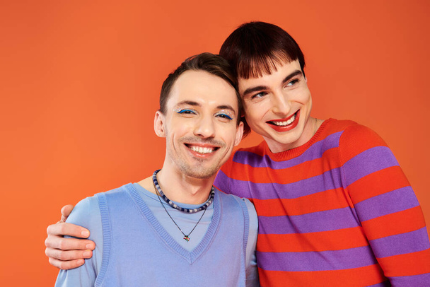 merry attractive gay friends with vivid makeup posing together on orange backdrop, pride month - Photo, Image