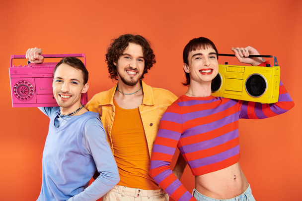 three joyous appealing gay friends in vivid attire posing with tape recorders, pride month - Фото, изображение