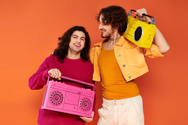 two cheerful attractive gay friends in vibrant clothes posing with tape recorders, pride month - Photo, Image