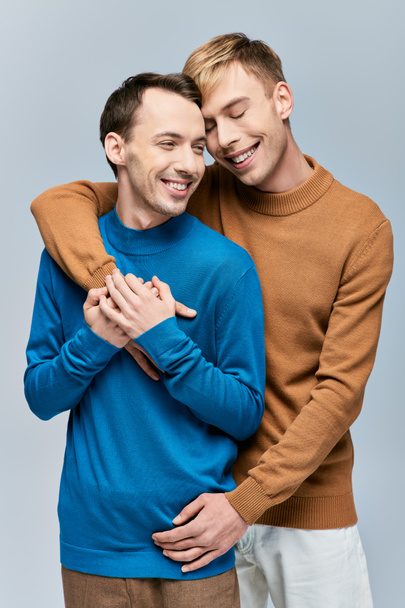 Двое мужчин в повседневной одежде стоят вместе, обнимая друг друга в любящих объятиях. - Фото, изображение