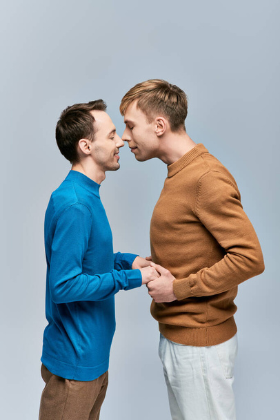 Deux jeunes hommes, un couple gay aimant, se tiennent ensemble en tenue décontractée sur fond gris. - Photo, image