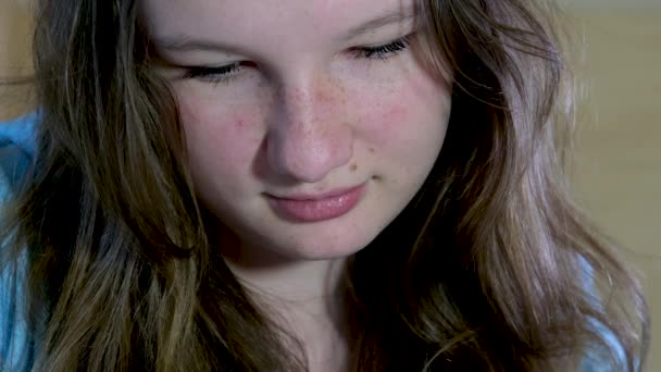 girl tilted hair and reads something on the phone or in a book close-up face of young young woman teenager against backdrop of bedroom with artificial lighting lamp evening at home to spend alone - Footage, Video