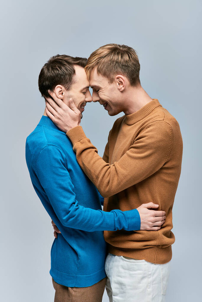 Una pareja gay amorosa con atuendo casual posando sobre un fondo gris. - Foto, imagen