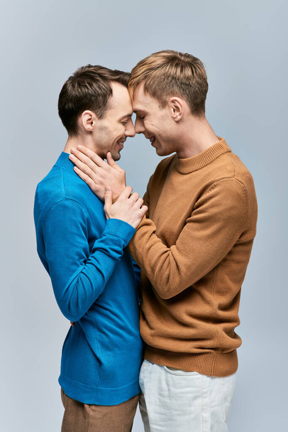 Двое мужчин в повседневной одежде обнимают друг друга, стоя бок о бок на сером фоне. - Фото, изображение