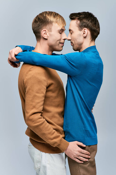 カジュアルな服装の2人の男性は,灰色の背景で互いに腕を並べて立っています.. - 写真・画像