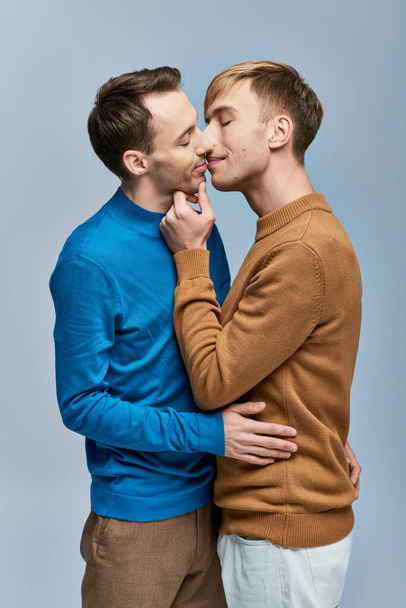 Ein liebevolles schwules Paar in lässiger Kleidung steht Seite an Seite vor grauem Hintergrund. - Foto, Bild