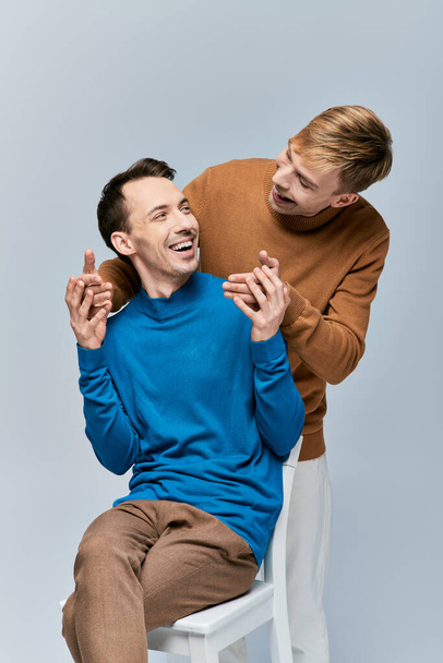 Двоє чоловіків у повсякденному вбранні сидять на білому стільці, ділячись сміхом і особливим моментом. - Фото, зображення