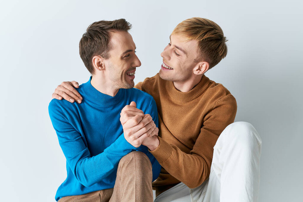 Dos hombres con atuendo casual compartiendo un momento de alegría en un fondo gris. - Foto, Imagen