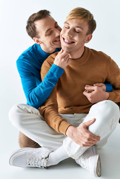 Two men sit on the ground, smiling happily as a loving gay couple in casual attires. - Фото, изображение