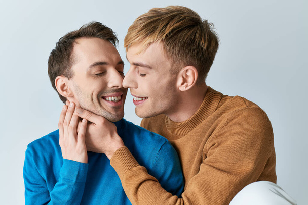 A loving gay couple in casual attires sharing a warm hug on a gray backdrop. - Photo, Image