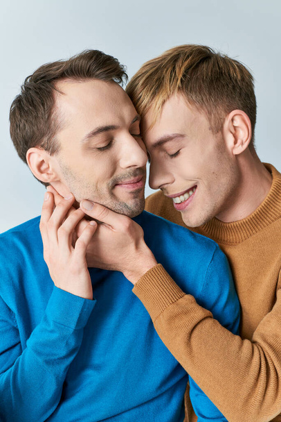 Два человека нежно обнимаются, любящая гей-пара в повседневной одежде, на сером фоне. - Фото, изображение