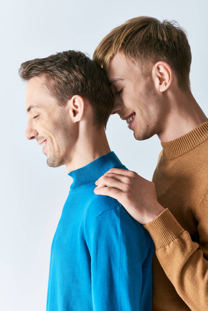 Dos hombres, una pareja gay amorosa, se paran uno al lado del otro con atuendo casual en un fondo gris. - Foto, Imagen
