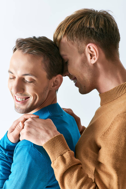 A loving gay couple in casual attire standing together on a gray backdrop. - Foto, afbeelding