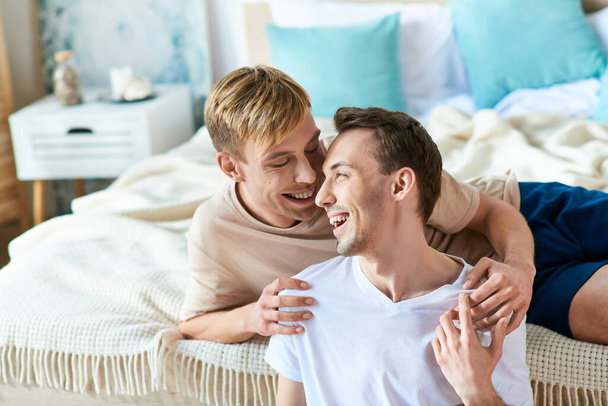 Deux hommes en tenue décontractée sont entrelacés sur un lit, respirant confort et connexion. - Photo, image
