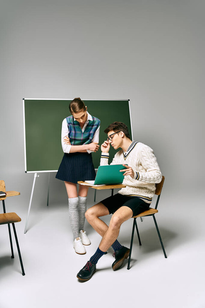 Ένας άντρας και μια γυναίκα κάθονται μπροστά από ένα πράσινο πίνακα στο κολέγιο.. - Φωτογραφία, εικόνα