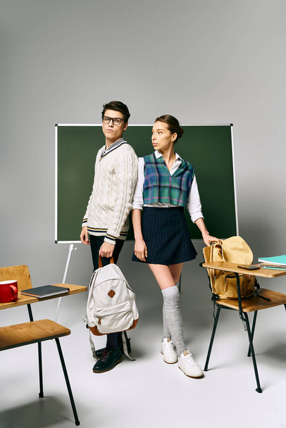 Два студента, мужчина и женщина, элегантно стоят перед зеленой школьной доской. - Фото, изображение