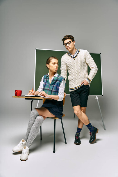 Stylish man and woman posing in front of green chalkboard in college. - Photo, Image