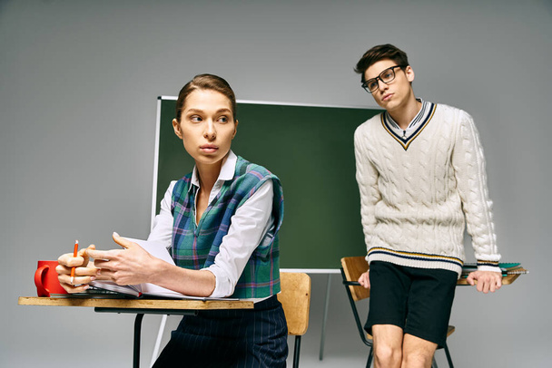 Элегантный мужчина и женщина в студенческой обстановке, сидящие за столом перед зеленой доской. - Фото, изображение