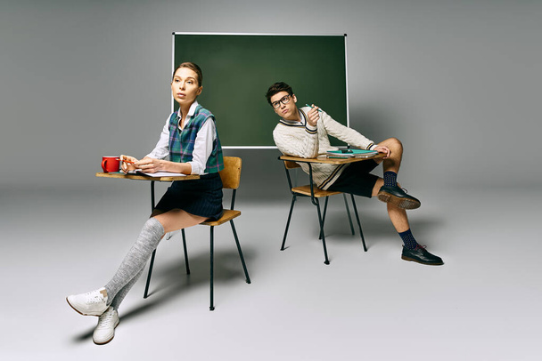 Dwóch stylowych studentów zajmujących się nauką przy biurku przed zieloną tablicą. - Zdjęcie, obraz