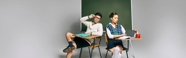 Δύο μαθητές, ένας άνδρας και μια γυναίκα, κάθονται σε ένα γραφείο μπροστά από ένα πράσινο πίνακα σε μια τάξη κολλεγίων. - Φωτογραφία, εικόνα
