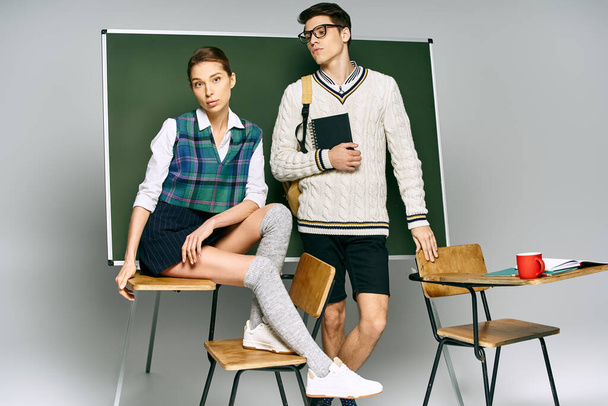 A stylish man and woman posing in front of a green board in a college setting. - Photo, Image