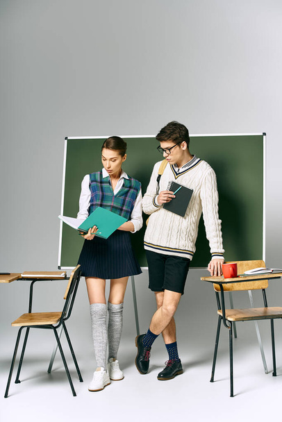 Stylowy mężczyzna i kobieta stoją przed zieloną tablicą w środowisku studenckim. - Zdjęcie, obraz