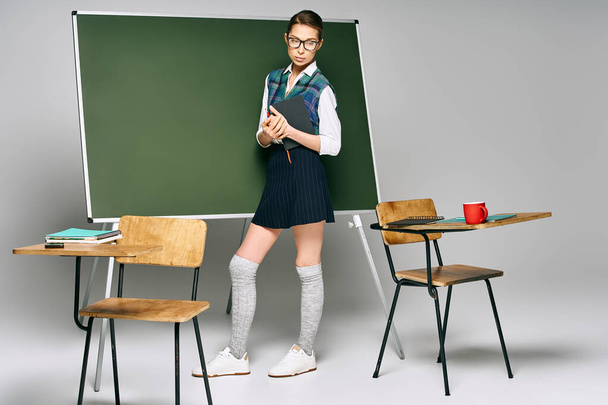 A female student in a school uniform stands before a green board. - Photo, Image