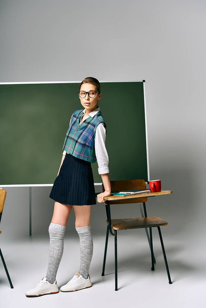 Eine Schülerin in Schuluniform steht selbstbewusst vor einer grünen Tafel. - Foto, Bild