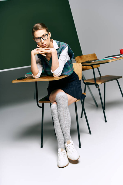Μια φοιτήτρια με στολή κάθεται σ 'ένα γραφείο και συλλογίζεται μπροστά σ' ένα πίνακα.. - Φωτογραφία, εικόνα