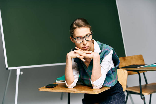 Estudante feminina em óculos, sentada em uma mesa, estudando na frente de um quadro. - Foto, Imagem