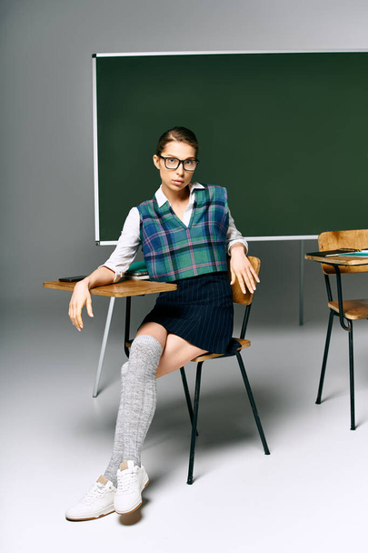 φοιτήτρια με στολή που κάθεται με πράσινη σανίδα στο κολέγιο. - Φωτογραφία, εικόνα