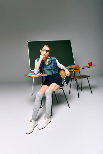 Молодая студентка в школьной форме, сидящая перед зеленой доской, погруженная в мысли. - Фото, изображение