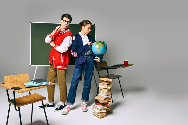 Dwóch studentów stojących przy biurku, otoczonych książkami i kulą ziemską. - Zdjęcie, obraz