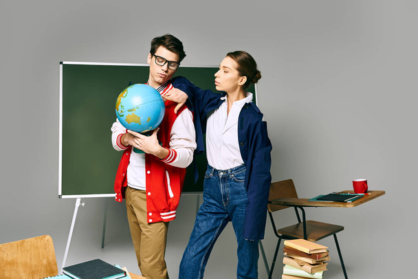Ένας άνδρας και μια γυναίκα μαθητές στέκονται μπροστά από μια τάξη, μελετώντας μια υδρόγειο σφαίρα.. - Φωτογραφία, εικόνα