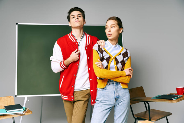 Two young people in casual attire stand confidently in front of a chalkboard in a college classroom. - Photo, Image