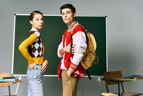 Un estudiante y una alumna con ropa casual se paran con confianza frente a un tablero verde en un salón de clases. - Foto, imagen