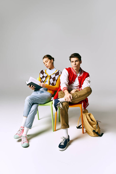 Młody mężczyzna i kobieta studenci w stylowych strojach siedzi na kolorowych krzesłach, swobodnie pozowanie. - Zdjęcie, obraz