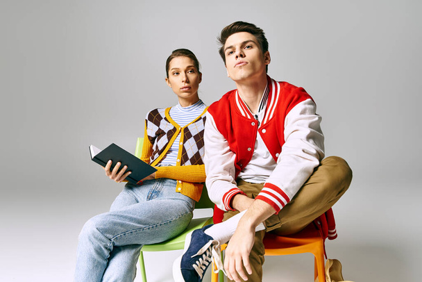 Ein junger Mann und eine junge Studentin sitzen auf Stühlen und halten ein Buch in der Hand. - Foto, Bild