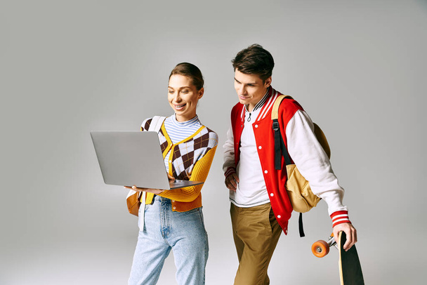 Üniversite ortamında dizüstü bilgisayar ve kaykay tutan genç erkek ve kız öğrenciler. - Fotoğraf, Görsel