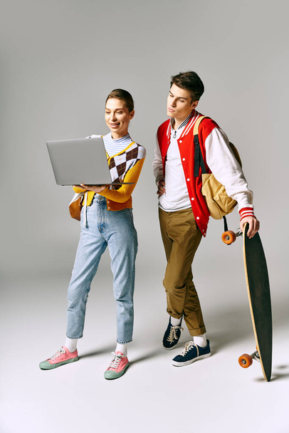 Two young individuals hold a laptop and skateboard in a classroom setting. - Photo, Image