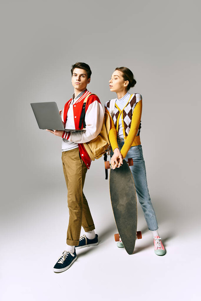 Jonge mannelijke en vrouwelijke studenten houden laptop en skateboard vast. - Foto, afbeelding