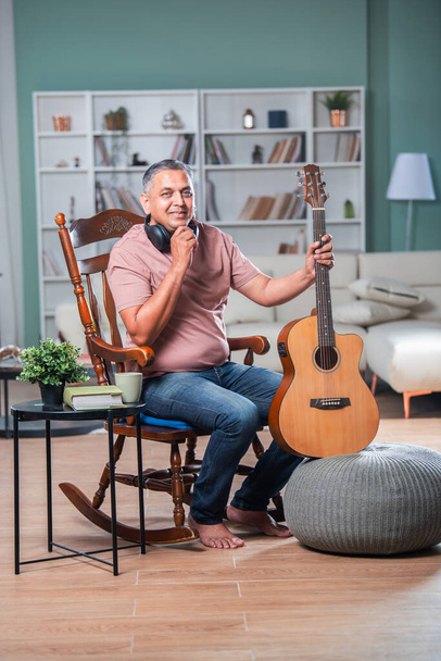 Indian asian mid age man with grey hair playing acaustic guitar in living room - Photo, Image