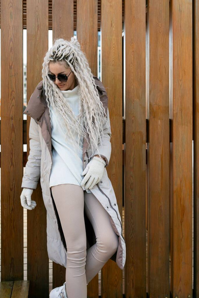 Een vrouw met lang wit haar staat in een luxe bontjas. De vrouwenharen vallen langs haar rug als ze elegant poseert in de warme winterkleding. - Foto, afbeelding