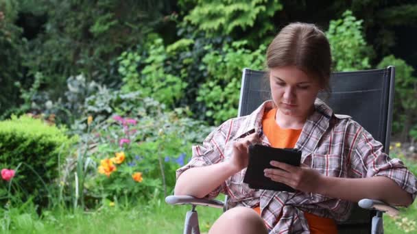 Young woman reading e-book in garden - Séquence, vidéo