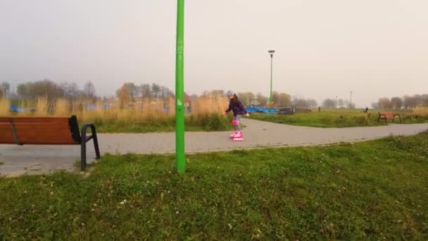 Вісім років дівчина в колінах і ліктях навчається кататися на роликових ковзанах на відкритому повітрі в міському парку. Малюк насолоджується активним спортом, широким кутом зору. Навчання хобі активного дозвілля молодіжної культури - Кадри, відео